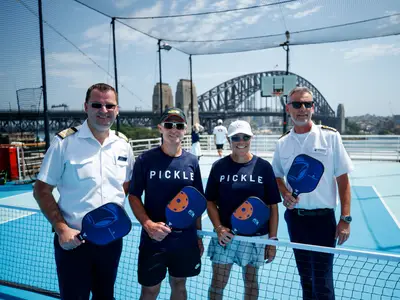 Vier Personen mit Pickleball-Schlägern posieren auf dem Sportdeck an Bord der Noordam, im Hintergrund ist die Sydney Harbour Bridge zu sehen.