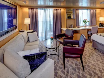 Blick in die geräumige Neptune Suite an Bord der Noordam mit stilvoller Einrichtung, Sofa, Sesseln und Balkonfenster.