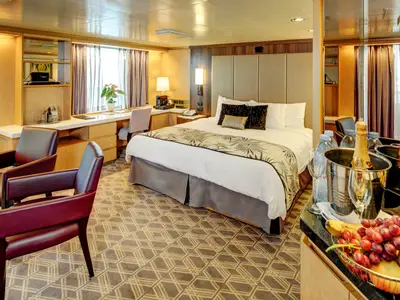Eine geräumige Neptune Suite an Bord der Noordam mit einem großen Doppelbett, Sitzecke und Sektkühler im Vordergrund.
