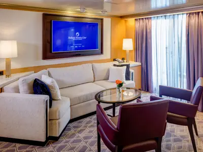 Einladender Wohnbereich einer Suite an Bord der Noordam mit Sofa, zwei roten Ledersesseln und einem Fernseher.