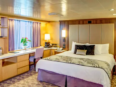 Blick in die gemütliche Neptune Suite an Bord der Noordam mit einem Doppelbett und Schreibtisch vor dem Fenster.