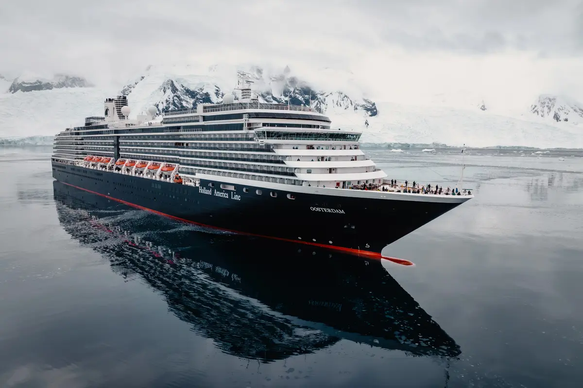 Die Oosterdam der Holland America Line fährt durch ruhiges, spiegelndes Wasser vor den schneebedeckten Gletschern der Antarktis.