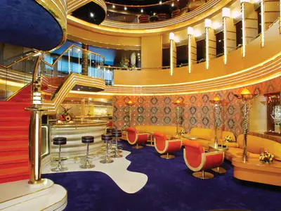 Das farbenfrohe Atrium an Bord der Oosterdam mit einer Bar, roten Sesseln auf blauem Teppich und einer geschwungenen Treppe.