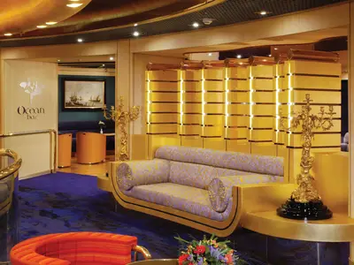 Ein elegantes, gemustertes Sofa mit goldenem Rahmen und reich verzierten Kandelabern in der Ocean Bar an Bord der Oosterdam.