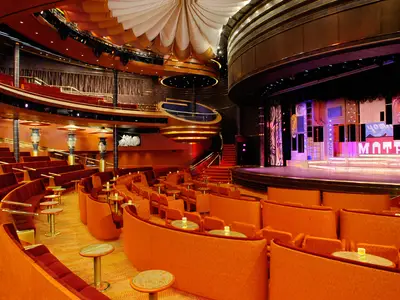 Blick in das prachtvolle, leerstehende Theater Vista Lounge an Bord der Oosterdam mit orangefarbenen Sitzen und großer Showbühne.