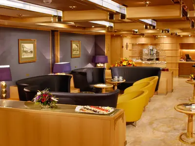 Die elegante Neptune Lounge an Bord der Oosterdam bietet gemütliche Sessel, Holzelemente, warme Beleuchtung und kleine Snacks.