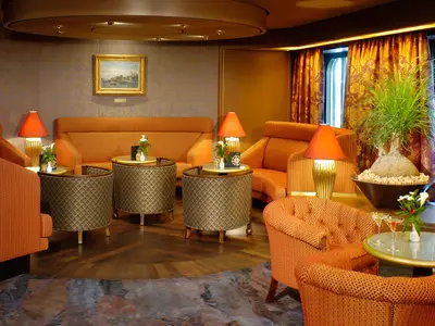 Gemütliche Explorer's Lounge an Bord der Oosterdam mit orangefarbenen Sofas, Sesseln, kleinen Tischen und warmer Beleuchtung.