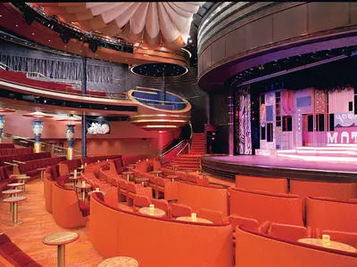 Ein Blick in das mehrstöckige Theater an Bord der Oosterdam mit roten Sesseln, kleinen Tischen und einer beleuchteten Bühne.