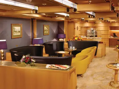 Die gemütliche Neptune Lounge an Bord der Oosterdam mit dunklen Sofas, gelben Sesseln, Beistelltischen und Snack-Buffet.