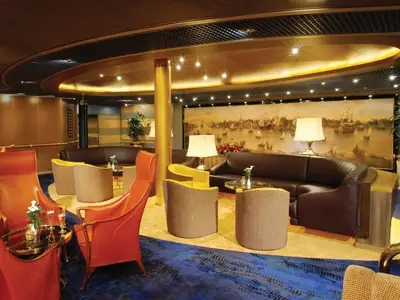 Blick in die warm beleuchtete Explorer's Lounge an Bord der Oosterdam mit Ledersofas und einem großen maritimen Gemälde im Hintergrund.