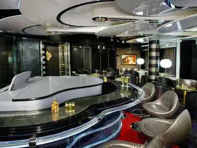 Die moderne Piano Bar an Bord der Oosterdam mit einem geschwungenen Tresen um einen weißen Flügel, silbernen Sesseln und gemütlicher Beleuchtung.