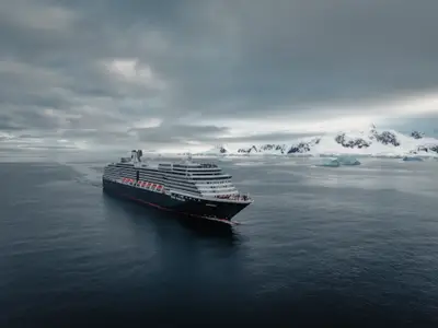 Luftaufnahme der Oosterdam, die in der Antarktis an schneebedeckten Bergen und Gletschern vorbeifährt.