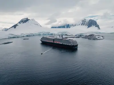 Eine Luftaufnahme zeigt das Kreuzfahrtschiff Oosterdam in einem antarktischen Fjord umgeben von schneebedeckten Bergen und Gletschern.