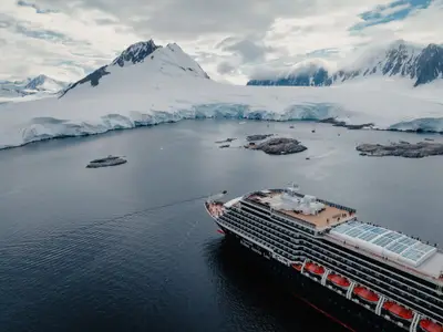 Luftaufnahme der Oosterdam vor einer gigantischen Kulisse aus Gletschern und schneebedeckten Bergen in der eisigen Antarktis.