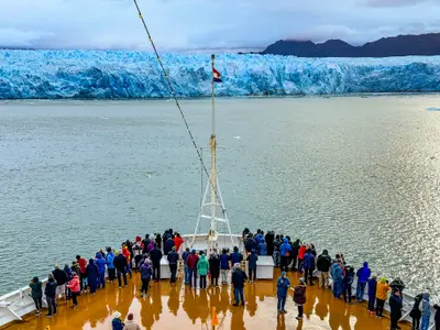 Passagiere auf dem Außendeck der Oosterdam beobachten eine riesige blaue Gletscherwand vom Schiff aus.