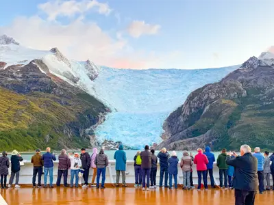Passagiere an Bord der Oosterdam blicken vom Außendeck auf einen riesigen, blau schimmernden Gletscher in Chile.