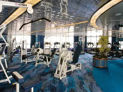 Das gut ausgestattete Fitnesscenter an Bord der Oosterdam bietet Kraft- und Kardiogeräte vor einer Fensterfront.