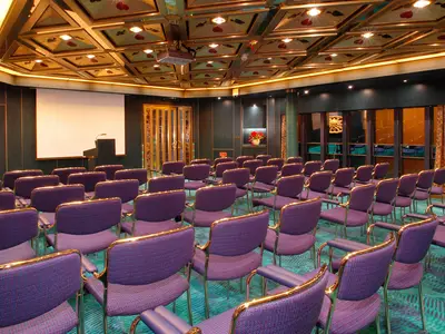 Blick auf die lila Stuhlreihen und die Präsentationsleinwand im Hudson Room an Bord der Oosterdam.