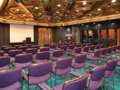 Einblick in den klassisch gestalteten Hudson Room an Bord der Oosterdam mit zahlreichen violetten Stühlen und Präsentationsleinwand.