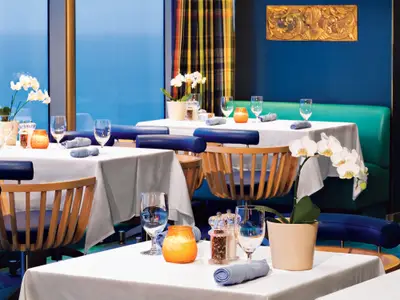 Gedeckte Tische mit weißen Tischtüchern, Orchideen und blauen Stühlen im Restaurant an Bord der Oosterdam.