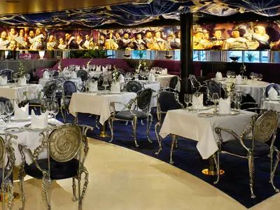 Elegant gedeckte Tische im Pinnacle Grill Restaurant an Bord der Oosterdam mit prunkvollen Stühlen und einem historischen Wandgemälde.