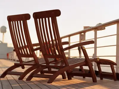 Zwei klassische Liegestühle aus Holz auf dem Außendeck an Bord der Oosterdam im warmen Abendlicht.