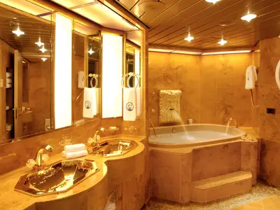 Das goldglänzende Badezimmer der Pinnacle Suite an Bord der Oosterdam mit Doppelwaschbecken und großem Whirlpool.