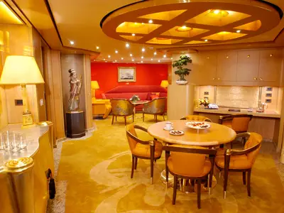 Blick in die edle Pinnacle Suite an Bord der Oosterdam mit goldenem Teppich, rundem Esstisch und rotem Sofa.
