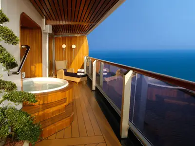 Balkon der Pinnacle-Suite an Bord der Oosterdam mit Holz-Whirlpool, Liegestuhl und Blick auf das blaue Meer am Abend.