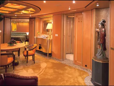 Innenansicht der eleganten Pinnacle Suite an Bord der Oosterdam mit einer asiatischen Skulptur und edlen Holzmöbeln.