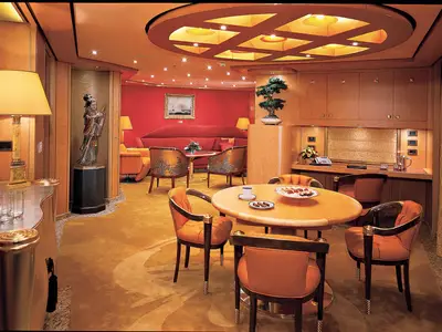 Blick in die luxuriöse Pinnacle Suite an Bord der Oosterdam mit einem Esstisch, gemütlichen Sesseln, asiatischer Kunst und warmem Licht.