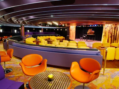 Die stilvolle Queen's Lounge an Bord der Oosterdam mit bunten Sesseln und einem Flügel auf der Bühne.