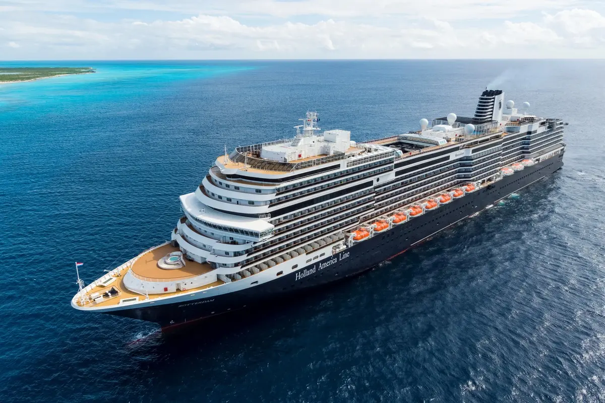 Luftaufnahme des Kreuzfahrtschiffs Rotterdam von Holland America Line auf dem tiefblauen Meer vor einer tropischen Küste.