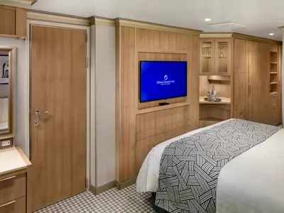 Blick in eine elegant eingerichtete Kabine an Bord der Rotterdam mit Doppelbett, TV und Holzmöbeln.