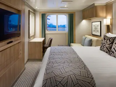 Eine gemütliche Außenkabine an Bord der Rotterdam mit einem Doppelbett, einem Sofa, Schreibtisch und Fenster mit Ausblick.