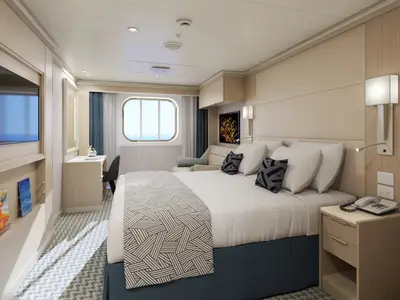 Modern eingerichtete Außenkabine mit großem Bett, Schreibtisch und rundem Meerblick-Fenster an Bord der Rotterdam.