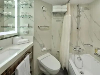 Helles, modernes Badezimmer an Bord der Rotterdam mit weißer Marmorwand, Waschbecken, Toilette und Badewanne mit Duschvorhang.