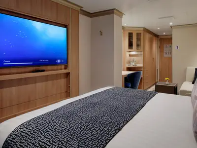 Innenansicht einer stilvollen Kabine an Bord der Rotterdam mit großem Flachbildfernseher, Bett und Holzmöbeln.