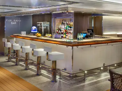 Blick auf die moderne Panorama Bar an Bord der Rotterdam mit weißen Barhockern an einer eleganten Theke.