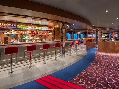 Die elegante Bar an Bord der Rotterdam mit einer Reihe von roten Barhockern, einer beleuchteten Theke und gemustertem Teppich.