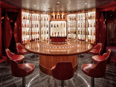Die Whisky-Bar "Notes" an Bord der Rotterdam zeigt einen runden Holztisch mit roten Ledersesseln und Regale voller edler Flaschen im Hintergrund.