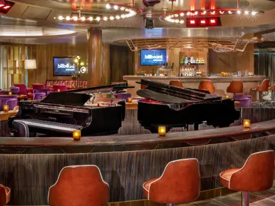 Innenansicht der Billboard Onboard Musikbar an Bord der Rotterdam mit zwei gegenüberstehenden Klavieren und warm beleuchteter Bar.