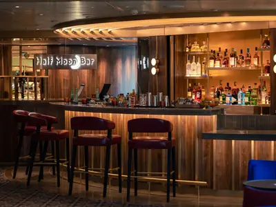 Einblick in die elegante Half Moon Bar an Bord der Rotterdam mit roten Barhockern an einer geschwungenen Holztheke und warmen Lichtinstallationen.