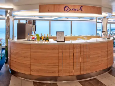 Die modern gestaltete Bar Quench an Bord der Rotterdam mit einer runden Holztheke, Getränken und Meerblick im Hintergrund.