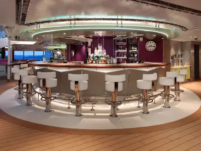 Eine runde Bar an Bord der Rotterdam mit weißen Barhockern, einer beleuchteten Deckenkuppel und lila Akzenten.
