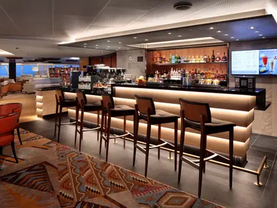 Die stilvolle Kaffeebar des Explorations Cafe an Bord der Rotterdam mit edlen Holz-Barhockern und einladender Beleuchtung.