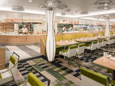 Das helle Lido Market Buffet-Restaurant an Bord der Rotterdam mit gruen-weissen Stuehlen, gedeckten Tischen und Essensstationen.