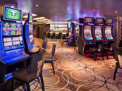 Spielautomaten mit bunten Displays und bequemen Stühlen im modern gestalteten Casino an Bord der Rotterdam.