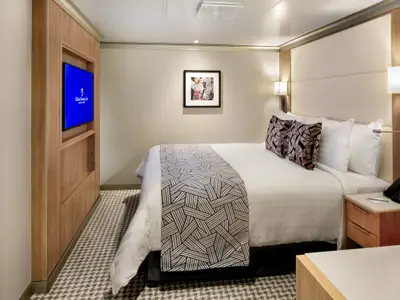 Blick in eine modern eingerichtete Innenkabine an Bord der Rotterdam mit einem großen Doppelbett, Fernseher und elegantem Holzdekor.