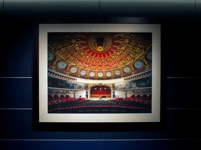 Ein gerahmtes Foto eines prachtvollen, klassisch gestalteten Theatersaals mit roter Decke an Bord der Rotterdam.